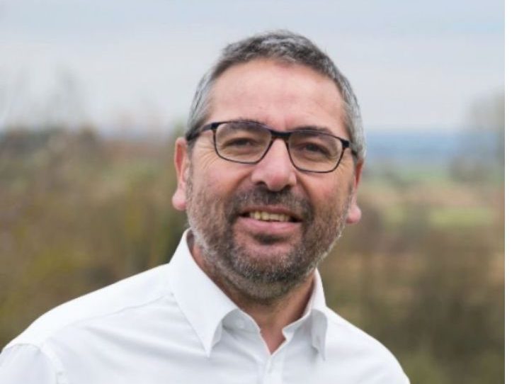 Christophe LEMARCHAND Homme souriant portant des lunettes, avec un paysage flou en arrière-plan.